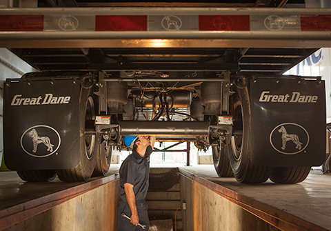 A male mechanic in a blue hard hat working on the undercarriage of a Great Dane trailer